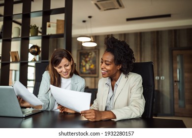 Two business woman sitting next to each other, holding and looking at some new documents.