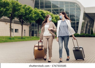 Two Business Women In Protective Masks With Suitcases Go To The Airport. Young Women Near Airport, Opening Air Travel, Travel Concept. Business Trips During Coronavirus Quarantine