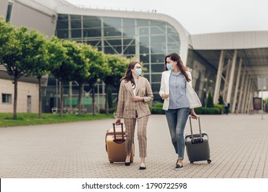 Two Business Women In Protective Masks With Suitcases Go To The Airport. Young Women Near Airport, Opening Air Travel, Travel Concept. Business Trips During Coronavirus Quarantine