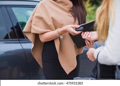 Two Business Women Standing Near The Car, Enter Into An Agreement On Sale And Purchase Of The Car. Stylish Woman In The Yard. Keys In Hand