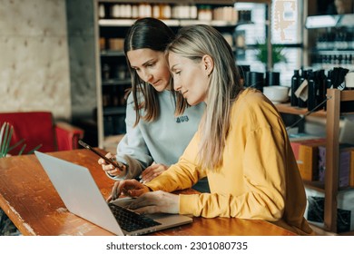 Two business women work behind the counter using electronic gadgets. - Powered by Shutterstock