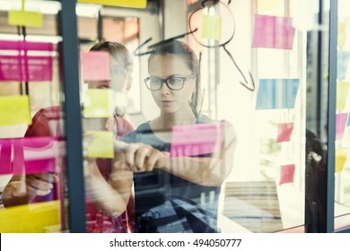 Two business women working together on wall glass with post it stickers. Modern startup office - Shutterstock ID 494050777