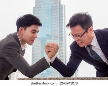 Two Businessman Are Clash Arm Wrestle On The Marble Table Front Of Skyscraper. Generation Gap Can Cause Conflicts In Work.