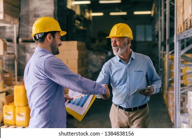 Two businessman with helmets on heads shaking hands for good finished job. Storage interior. - Powered by Shutterstock