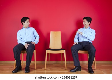 two businessman looking each other with a suspicion look, next to a red wall