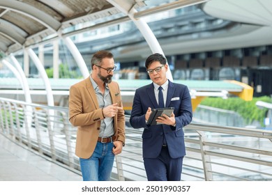 Two Businessman working corporate business and financial on digital tablet and discussion business plan during walking in the city. Business people entrepreneur partnership meeting outside office.