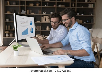 Two businessmen brothers twins working on analytics using computer, sit at desk, review sales statistics charts, graphs shown on pc monitor, discussing project revenue. Family business, partnership - Powered by Shutterstock