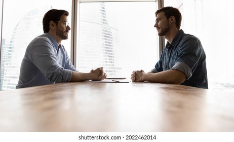 Two businessmen, business competitors, opponents sitting opposite at table with clasped hands in silent debate. Coworkers, partners having problem relationship. Corporate fight, competition concept