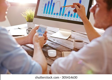 Two Businessmen Discussing Chart On Computer Monitor In Office