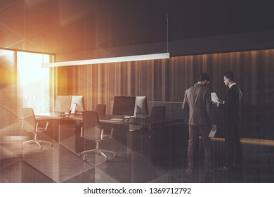 Two businessmen discussing documents in stylish wooden open space office with black computer tables and large window. Toned image double exposure blur
