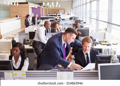 Two Businessmen Discussing Work In A Busy, Open Plan Office