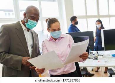 Two Businessmen With Face Mask Over Covid-19 Talk About A Business Document In The Office