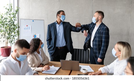 Two Businessmen In Face Masks Bumping Elbows During Corporate Meeting Standing In Modern Office. New Handshake Greeting, Etiquette For Business People During Coronavirus Pandemic