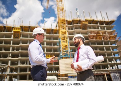 Zwei Geschäftsleute in Helmen, die auf dem Hintergrund der Gebäudestruktur sprechen 