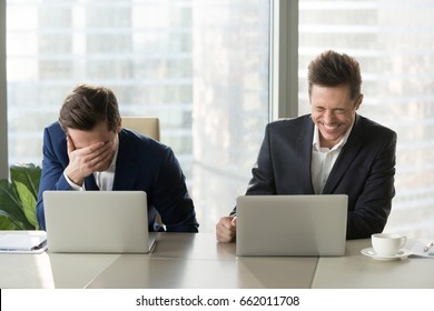 Two businessmen laughing out loud at workplace, office workers screaming with laughter and can not stop, funny positive emotions at work, cheerful colleagues having fun sitting at desk with laptops - Shutterstock ID 662011708