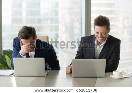 Two businessmen laughing out loud at workplace, office workers screaming with laughter and can not stop, funny positive emotions at work, cheerful colleagues having fun sitting at desk with laptops