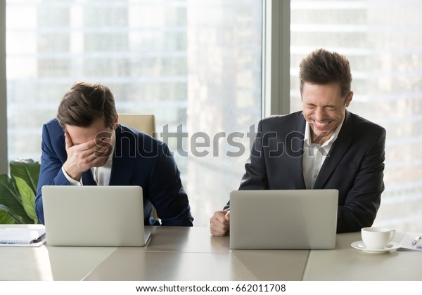 Two businessmen laughing out loud at workplace,
office workers screaming with laughter and can not stop, funny
positive emotions at work, cheerful colleagues having fun sitting
at desk with laptops