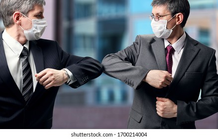 Two businessmen with a medical mask on their faces greet in a new way, striking with their elbows instead of a handshake. Social distance during the coronavirus epidemic