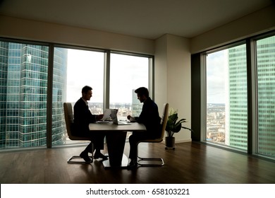 Two Businessmen Negotiating Sitting At Conference Table In Modern Office Interior With Big Full-length Window And City Buildings Outside, Business Partners Working Together, Preparing Business Offer