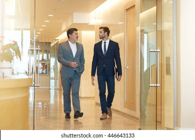 Two Businessmen, One Young And One Mature, Talking Seriously While Walking Together In A Modern Office Building Foyer