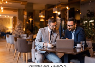 Two businessmen, professional managers using smartphone and laptop computer in co-working, checking corporate apps while sitting in city coffee shop or restaurant. Stylish men on meeting in coffee bar - Powered by Shutterstock