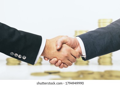 Two businessmen shake hands on the background of growing stacks of gold coins, making money concept, close up - Powered by Shutterstock