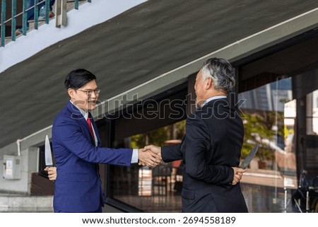 Two businessmen shake hands while one hides a knife behind his back, symbolizing betrayal, deceit, backstabbing, and the dangers of trust and dishonesty in business relationships.