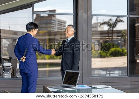 Two businessmen shake hands while one hides a knife behind his back, symbolizing betrayal, deceit, backstabbing, and the dangers of trust and dishonesty in business relationships.