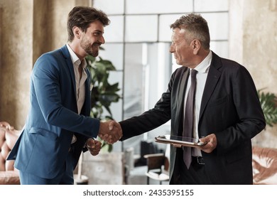 Two businessmen shaking hands in an office setting - Symbol of successful agreement and partnership. - Powered by Shutterstock