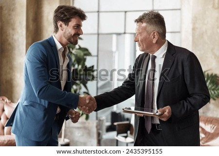 Two businessmen shaking hands in an office setting - Symbol of successful agreement and partnership.