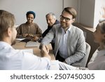 Two businessmen shaking hands seated at conference table, gesture of greeting, showing mutual respect, conclusion of commercial deal or agreement, sign of both parties accept terms discussed. Business