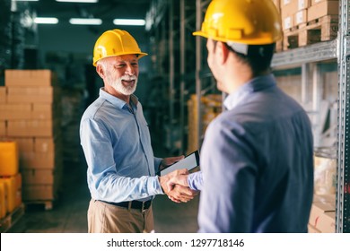 Two businessmen shaking hands for successful business while standing in warehouse. - Powered by Shutterstock