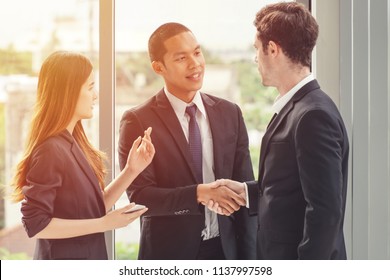 Two businessmen shaking hands with a woman secretary/translator standing on the side.