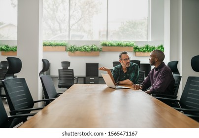 Two Businessmen Sitting At Boardroom Table For Meeting Discussing Information On Laptop With Copyspace