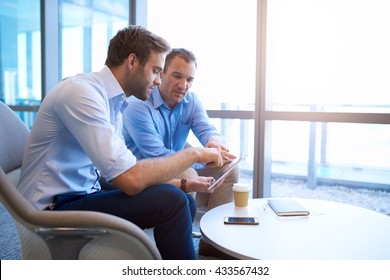 Two businessmen sitting in a bright modern office space, using a digital tablet in their discussions regarding a new collaboration - Shutterstock ID 433567432