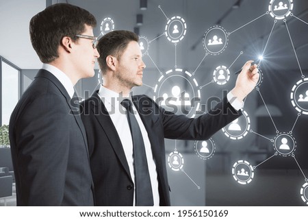 Two businessmen touching the multiple application hologram icons with coworking space in the background, social media and communication concept