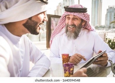Two businessmen with traditional emirates clothes meeting in Dubai - Senior and young adults having business in the UAE