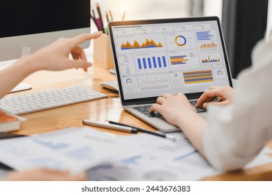 Two businesspeople or an accountant team are analyzing data charts, graphs, and a dashboard on a laptop screen in order to prepare a statistical report and discuss financial data in an office