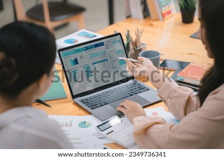 Two businesspeople or an accountant team are analyzing data charts, graphs, and a dashboard on a laptop screen in order to prepare a statistical report and discuss financial data in an office