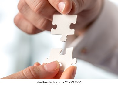 Two businesspeople fitting together matching interlocking puzzle pieces conceptual of teamwork and problem solving, closeup of their hands.
