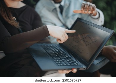 Two businesspeople focus on a laptop screen displaying financial graphs, collaborating while outdoors in a casual setting. - Powered by Shutterstock