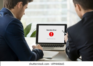 Two businesspeople looking at broken laptop screen with sudden system failure message, windows not working, hanging computer, critical fatal operation error with all data lost, close up rear view