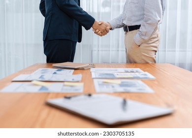 Two businesspeople shake hand after signing contract document to merge their partnerships in conference room and finalized pile of papers of financial report and data analysis on meeting table. Entity - Shutterstock ID 2303705135