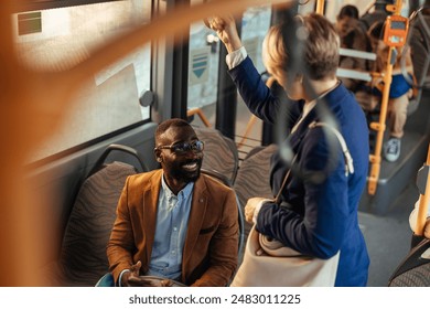 Two businesspeople, a young, good looking African-American man and a white woman with short hair, having a cheerful conversation on a public bus. - Powered by Shutterstock