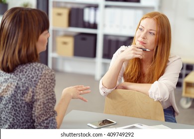 Two Businesswoman Having An Informal Meeting With One Sitting Relaxing On A Reversed Chair Listening To Her Colleague With A Pensive Expression