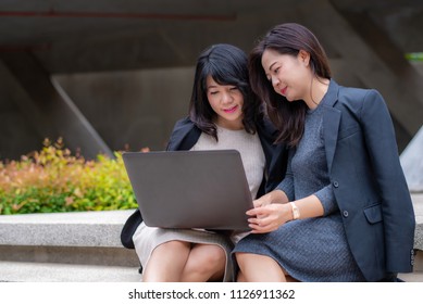Two businesswoman working together with laptop in front of their office building 