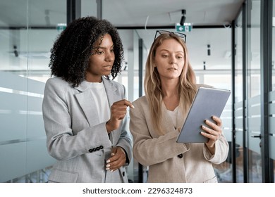 Two businesswoman working together using digital tablet pc and talking about a business project. Small creative diversity team of African American and blond females executives meeting work in office. - Powered by Shutterstock