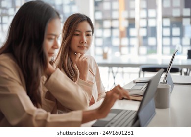 Two businesswomen collaborate on a project at the office, working together on laptops in a modern, professional environment. - Powered by Shutterstock