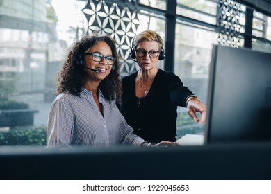 Two businesswomen cooperating while using computer and working in the office. Manager helping female colleague working on computer. Both wearing headset working in a call center. - Powered by Shutterstock