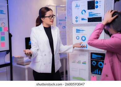 Two businesswomen are discussing and analyzing financial charts and graphs using a virtual reality headset in a modern office, exploring innovative ways to interpret data